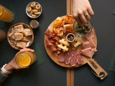 Un plateau posé sur une table avec assortiment de viandes, d’olives, de fromage et de pâtisseries. À côté: une corbeille de pain et des pâtisseries, ainsi que des boissons dans des verres.