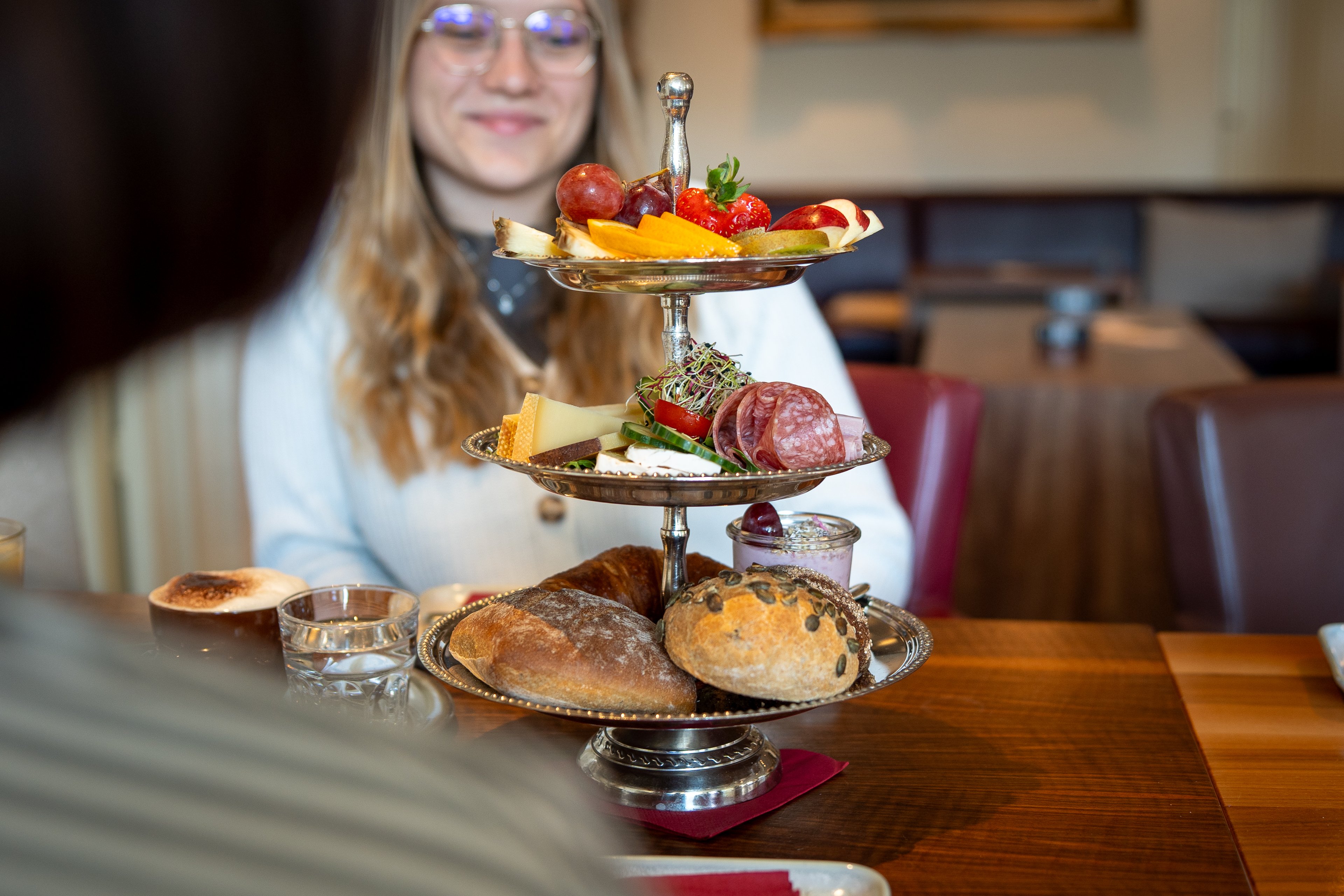 Auf einer dreistöckigen Etagère befinden sich Früchte, Käse, Salami und Brötchen.
