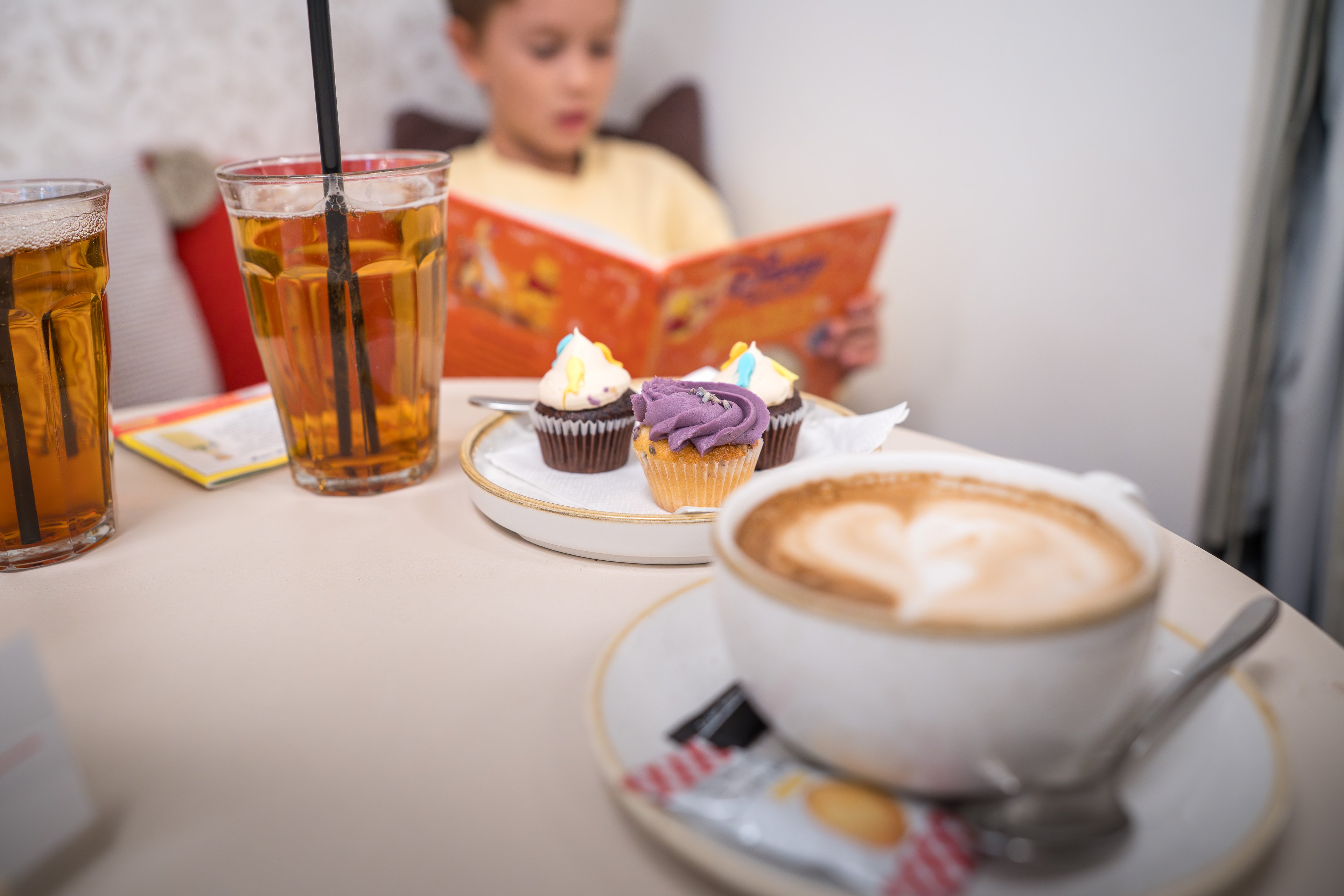 Cappuccino, Sirup auf dem Tisch, ein lesendes Kind im Hintergrund.  