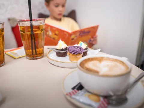 Cappuccino, Sirup auf dem Tisch, ein lesendes Kind im Hintergrund.