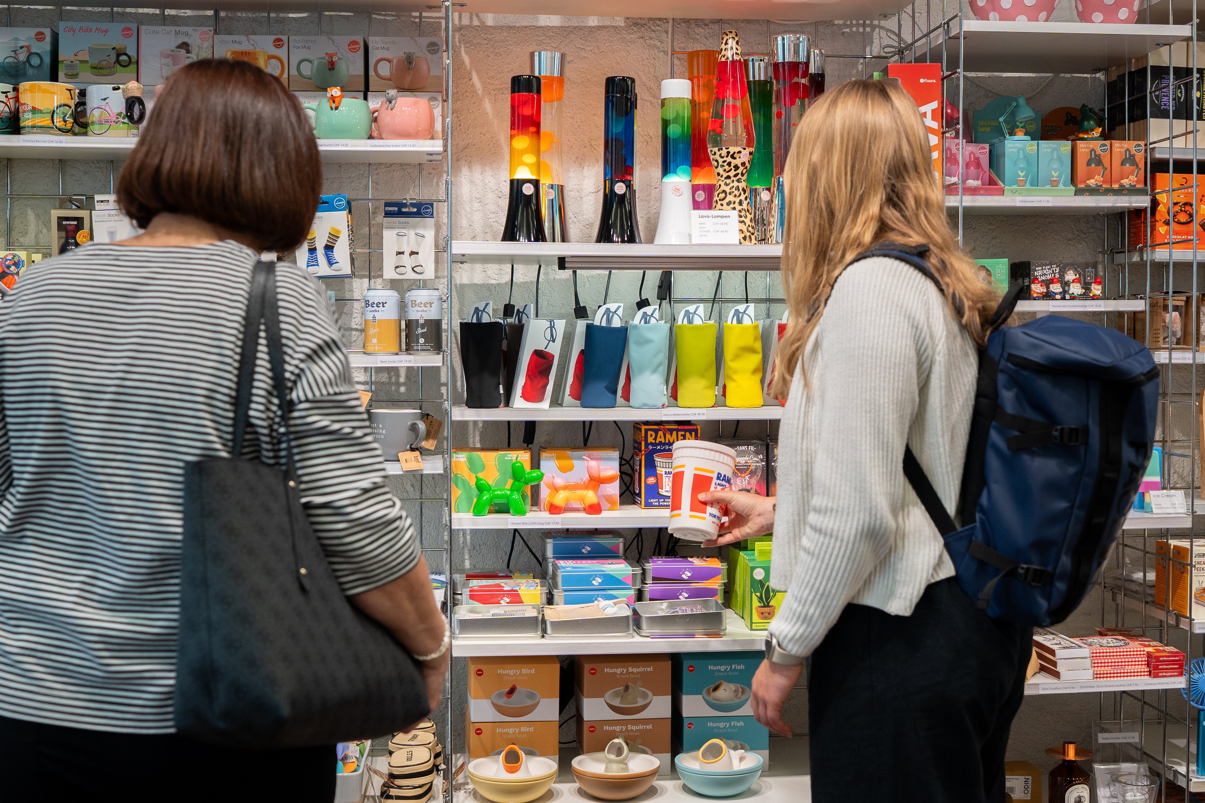 Zwei Personen stehen vor einem Regal mit vielen bunten, kleineren Produkten.