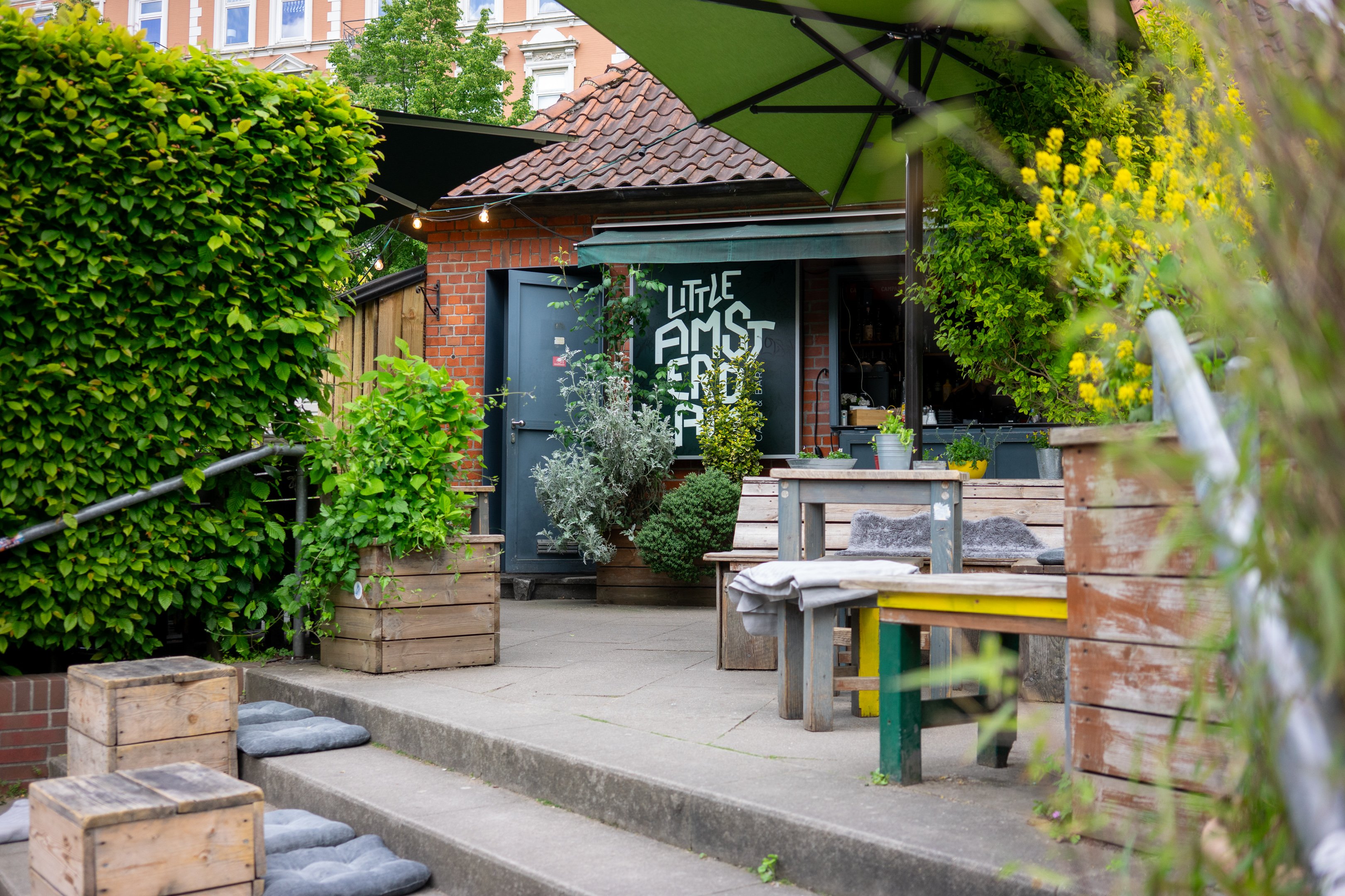 Blick auf die Terrasse des Bistro "Little Amsterdam" mit rustikalen Sitzmöglichkeiten und sehr viel Planzen.