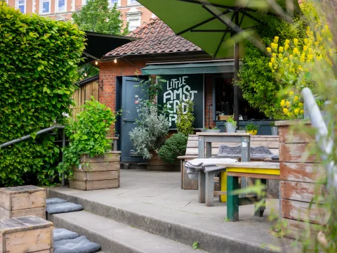Blick auf die Terrasse des Bistro "Little Amsterdam" mit rustikalen Sitzmöglichkeiten und sehr viel Planzen.