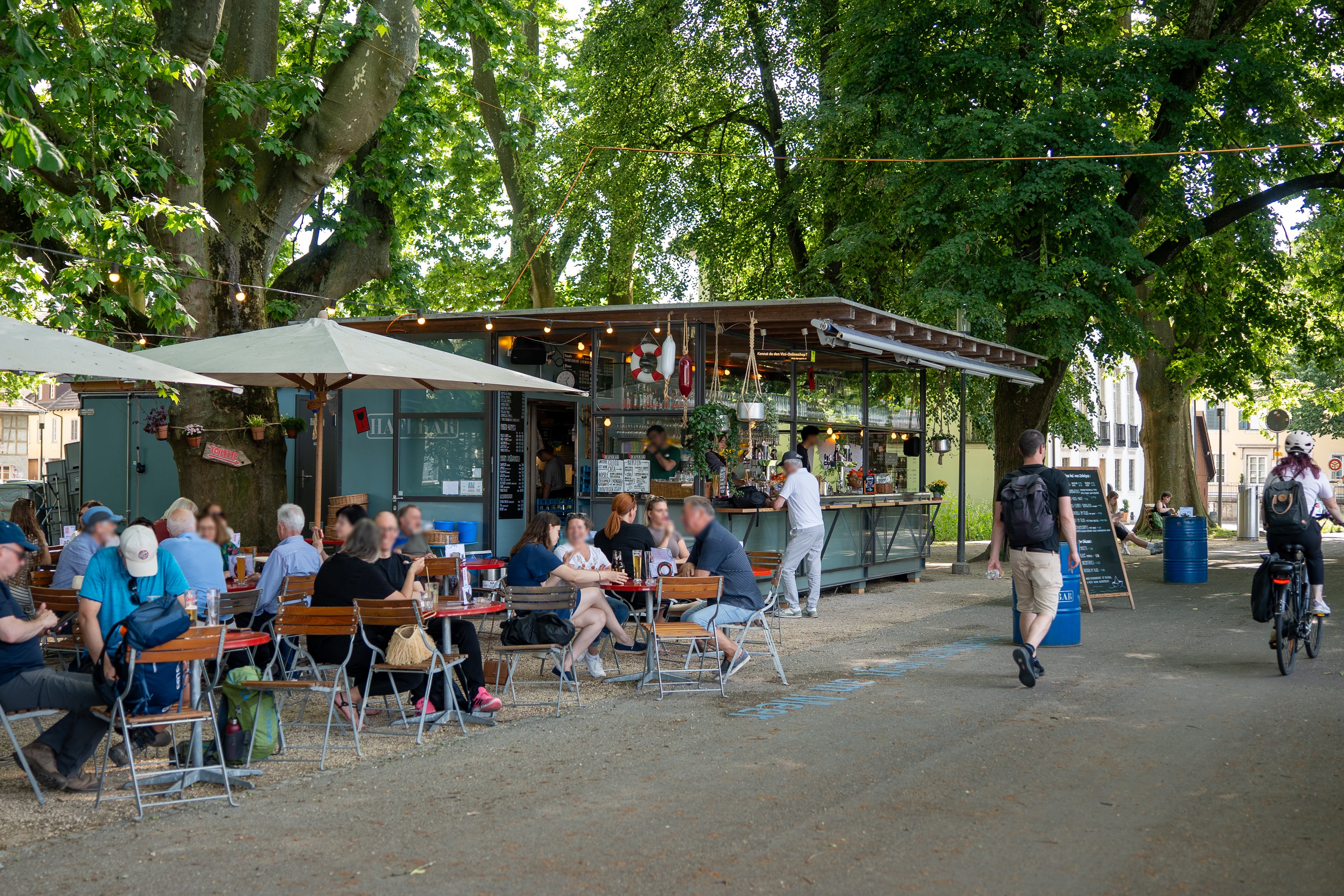 Eine Gartenwirtschaft mit Tischen, Sonnenschirmen und einer Bar.