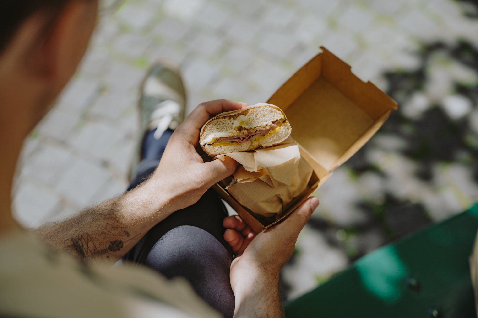 Une main tient un bagel coupé garni de viande et de fromage.