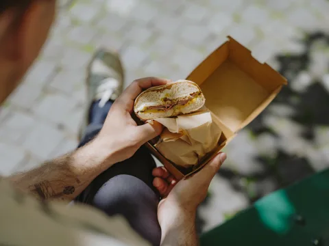 Une main tient un bagel coupé garni de viande et de fromage.