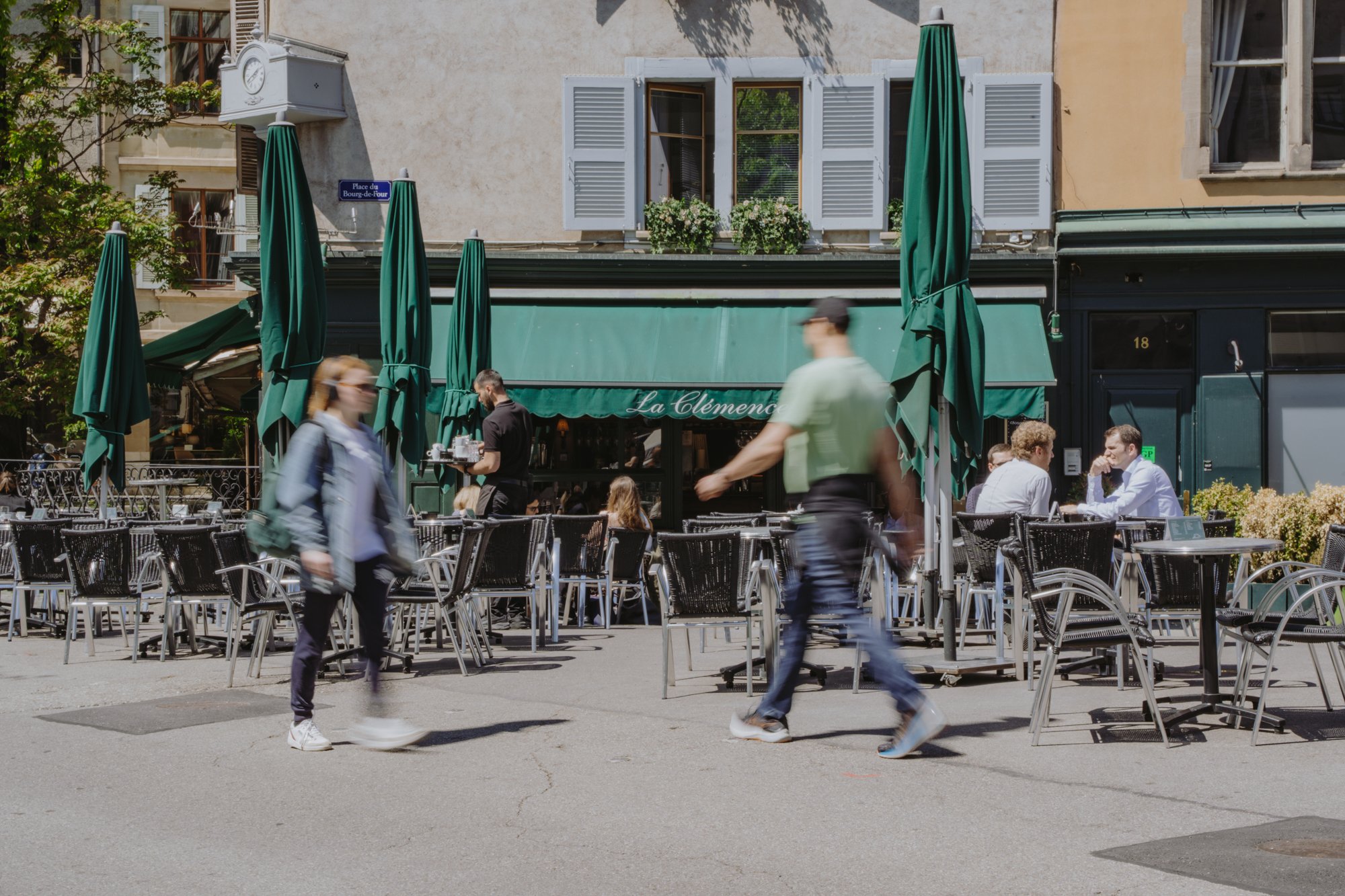 La terrasse extérieure du café genevois La Clémence, avec son auvent vert, sa clientèle détendue et des passants.