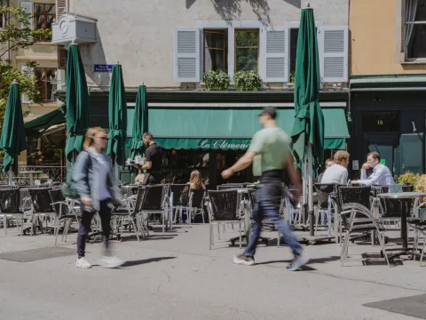 La terrasse extérieure du café genevois La Clémence, avec son auvent vert, sa clientèle détendue et des passants.