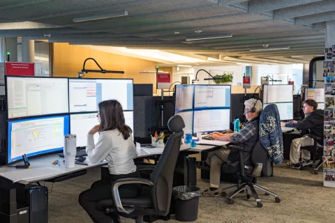 Ansicht in den Kommandoraum TOP SBB Cargo Schweiz, mit drei Mitarbeitern an ihren Schreibtischen vor zwei Reihen mit je zwei Bildschirmen.