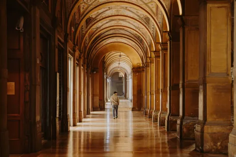 Person walking through an illuminated arcade in Bologna at night