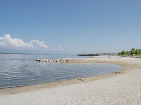 Une plage de sable avec de petites criques, une eau claire et un ciel à peine nuageux.