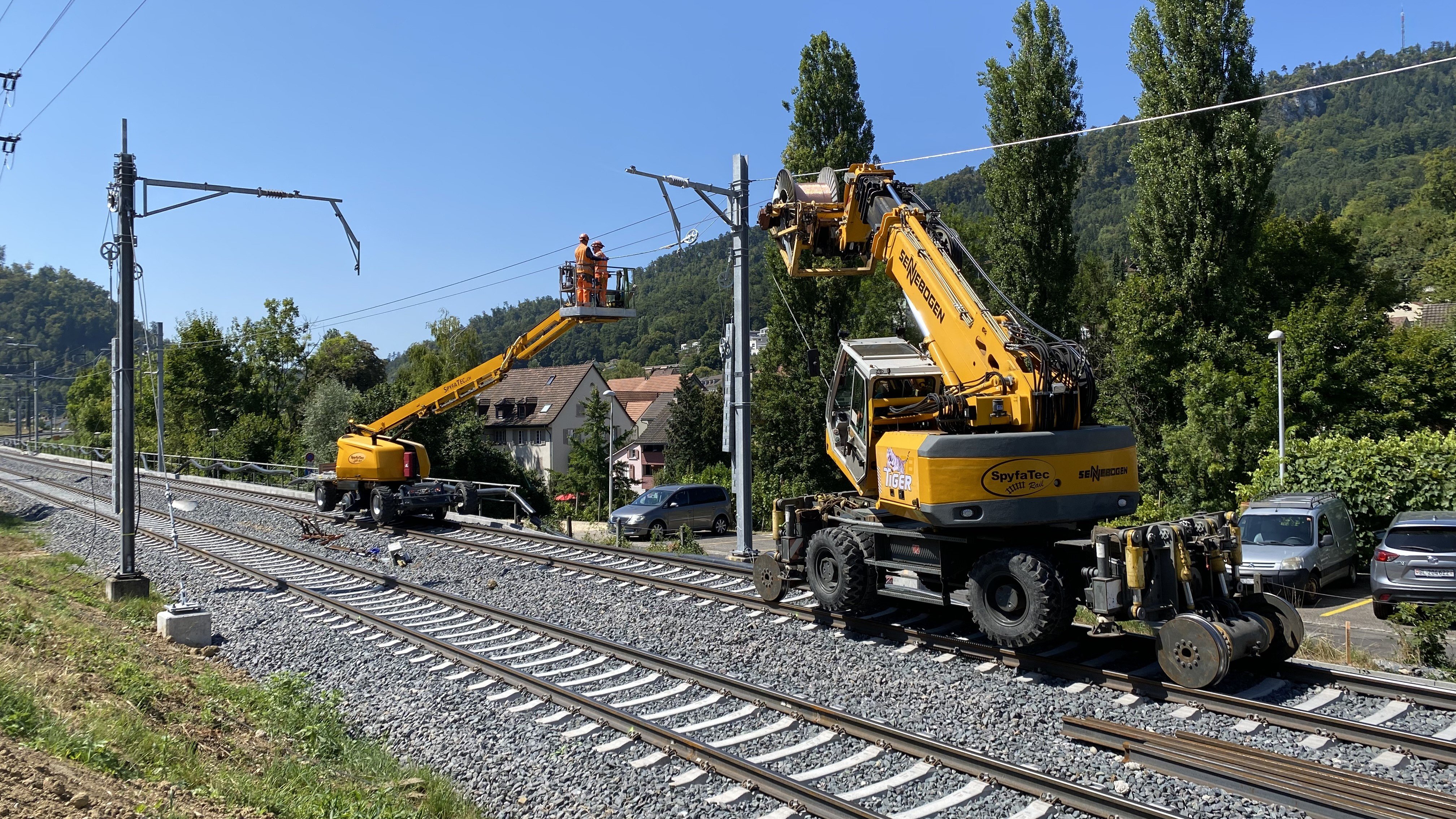 Deux véhicules à grue sur rail à partir desquels le personnel monte le fil de contact.