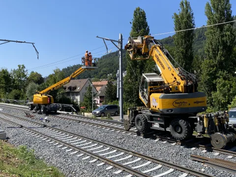 Deux véhicules à grue sur rail à partir desquels le personnel monte le fil de contact.