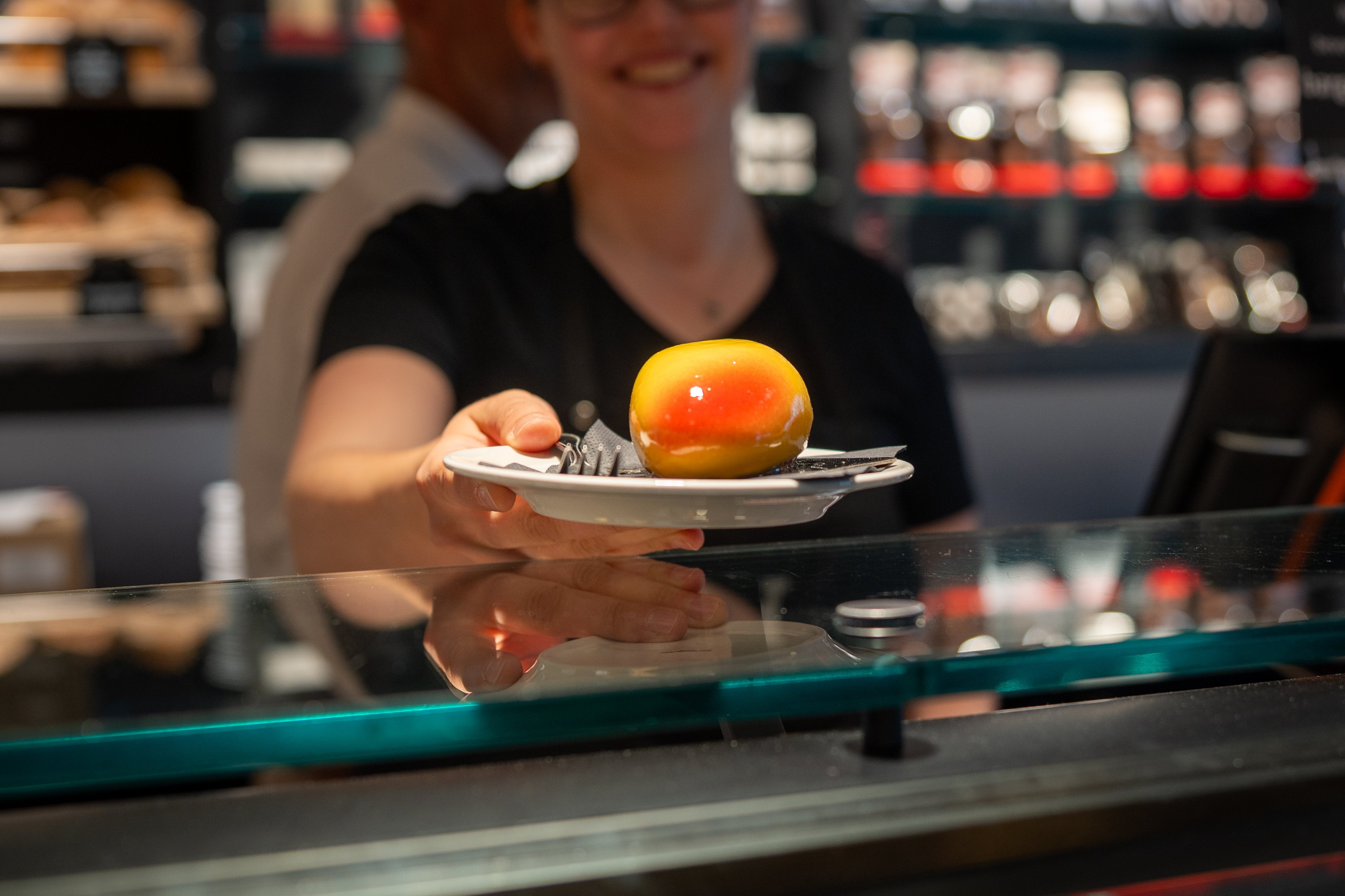 Auf einem Teller liegt eine glänzende Dessert-Kreation, die aussieht wie eine Mango.