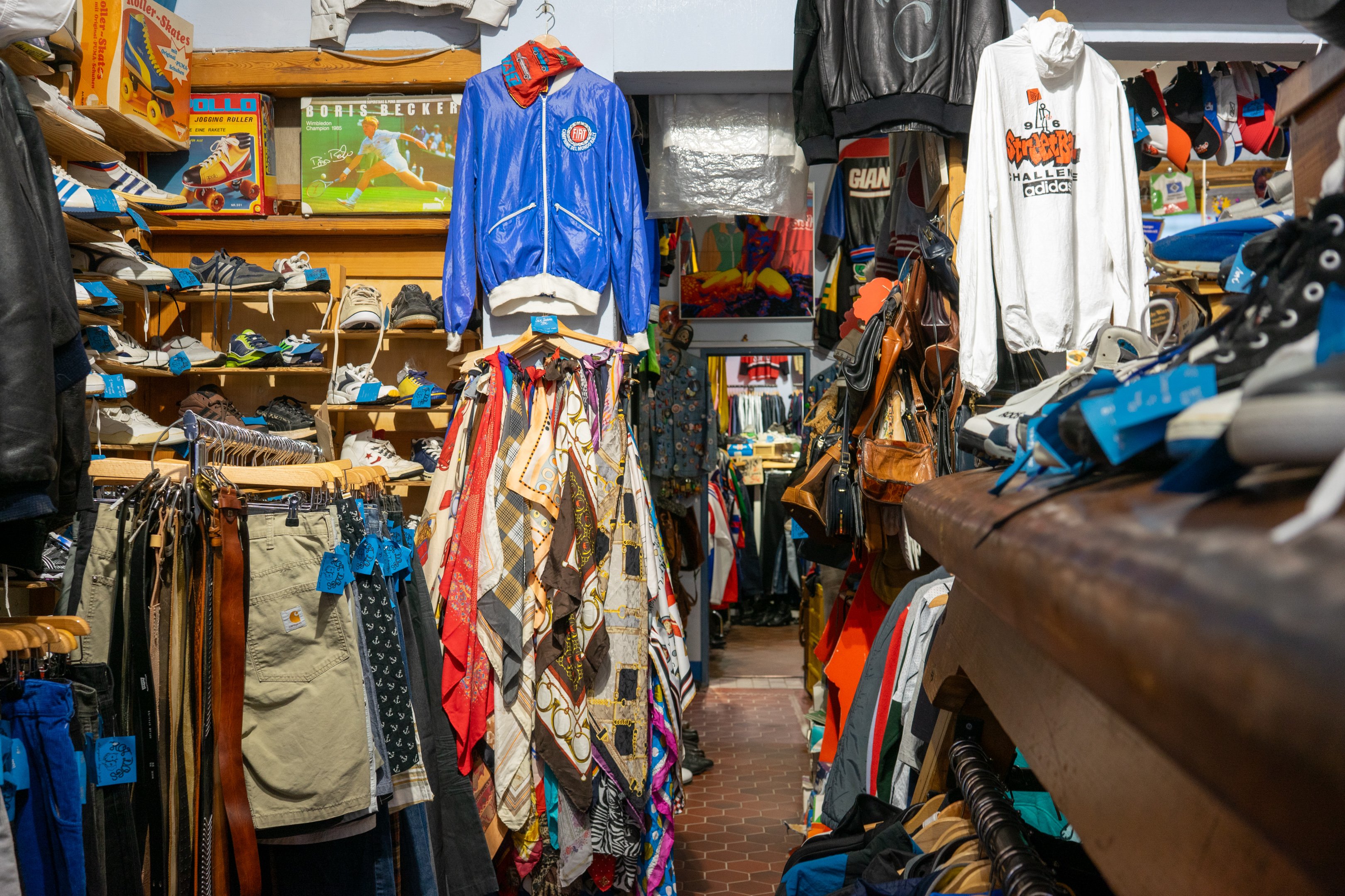 Einblick in einen vollgestopften Second Hand Shop wo Kleidungsstücke an den Wänden Händen in unterschiedlichen Farben.