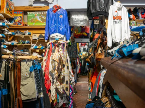 Einblick in einen vollgestopften Second Hand Shop wo Kleidungsstücke an den Wänden Händen in unterschiedlichen Farben.