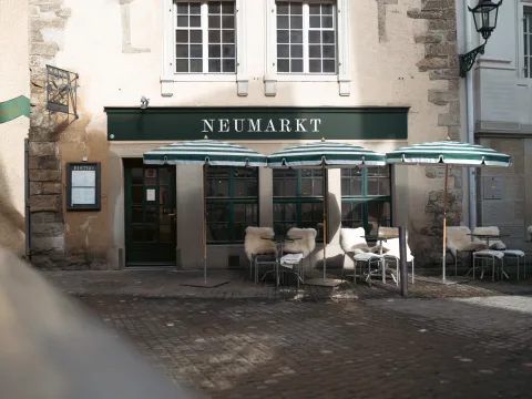 Un restaurant dont on voit le nom «Neumarkt» avec sa véranda, des sièges et des parasols.
