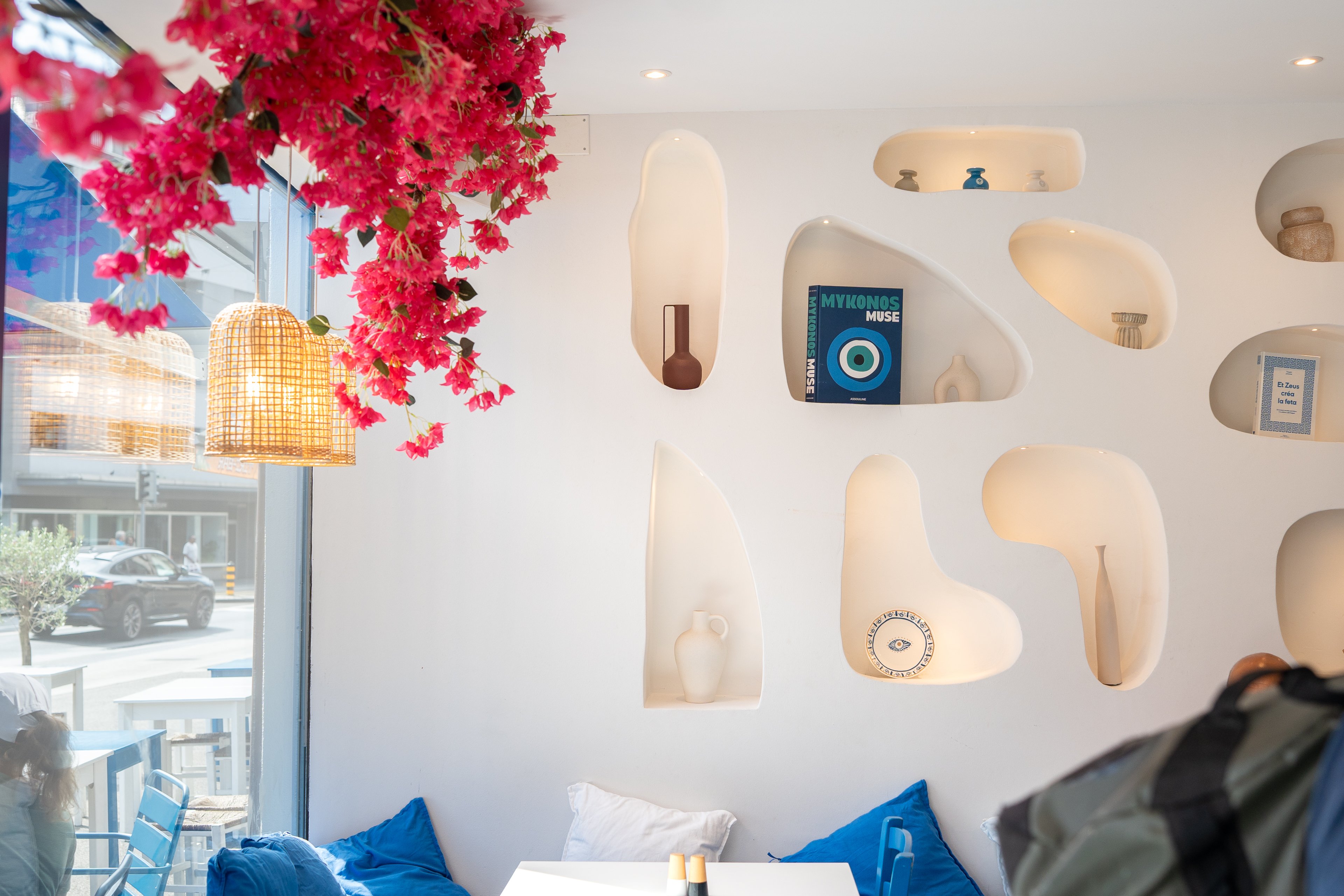 Veduta di una parete bianca all’interno di un ristorante, con nicchie in cui sono esposti diversi elementi decorativi. A sinistra si trova una grande finestra con vista sulla città, sopra la quale è appesa una decorazione floreale.