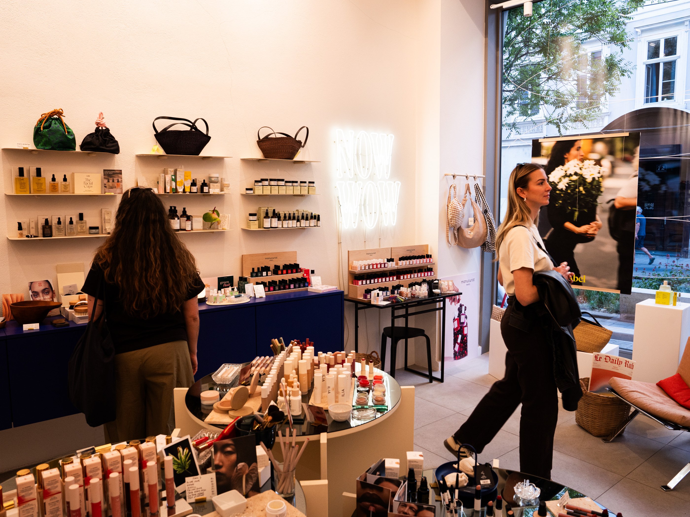 Due donne si trovano in un luminoso negozio di cosmetici circondate da prodotti di bellezza, profumi e mensole decorative a Vienna.