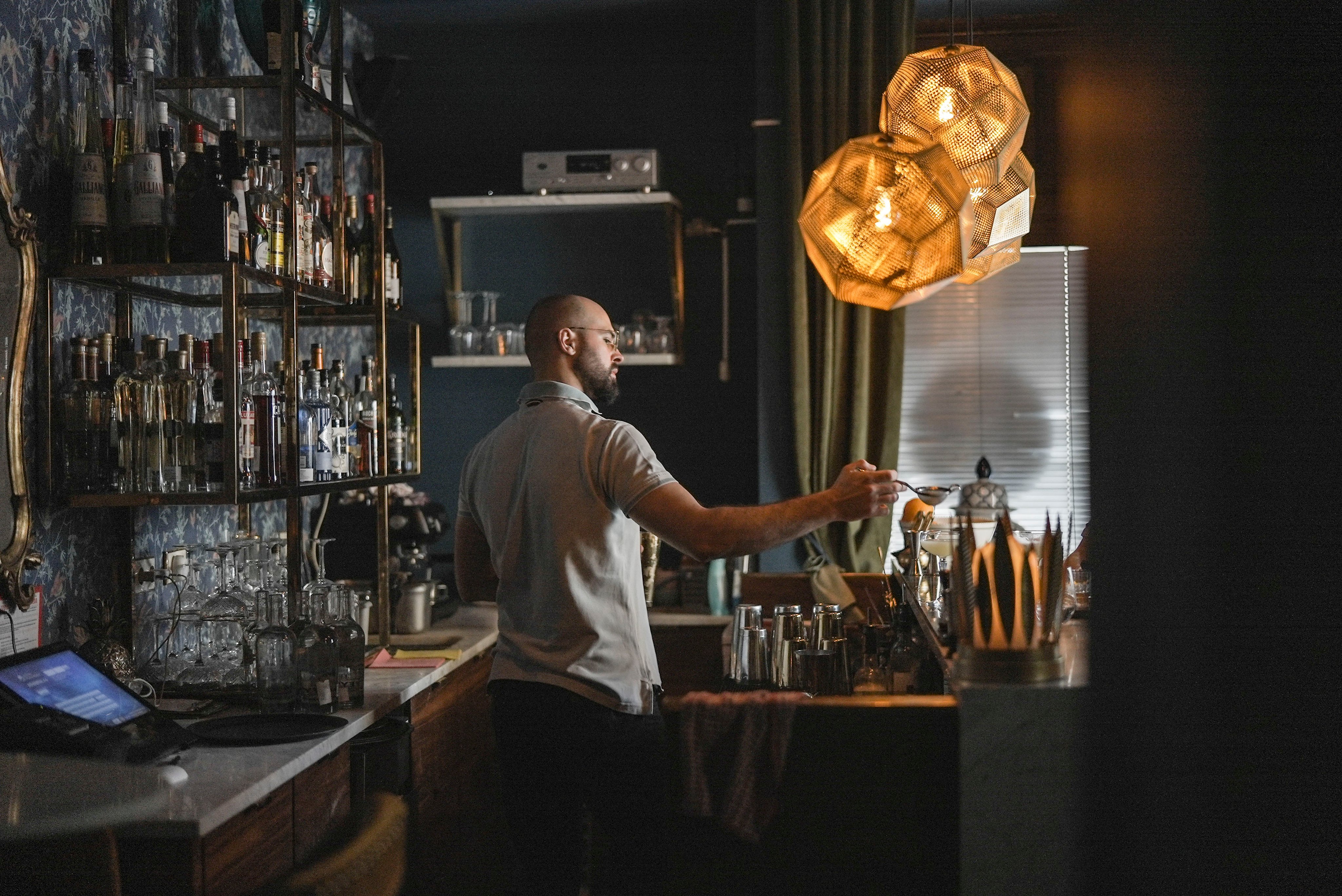 Der Bartender lässt hinter der Bar Saft durch ein Sieb ins Cocktailglas fliessen.