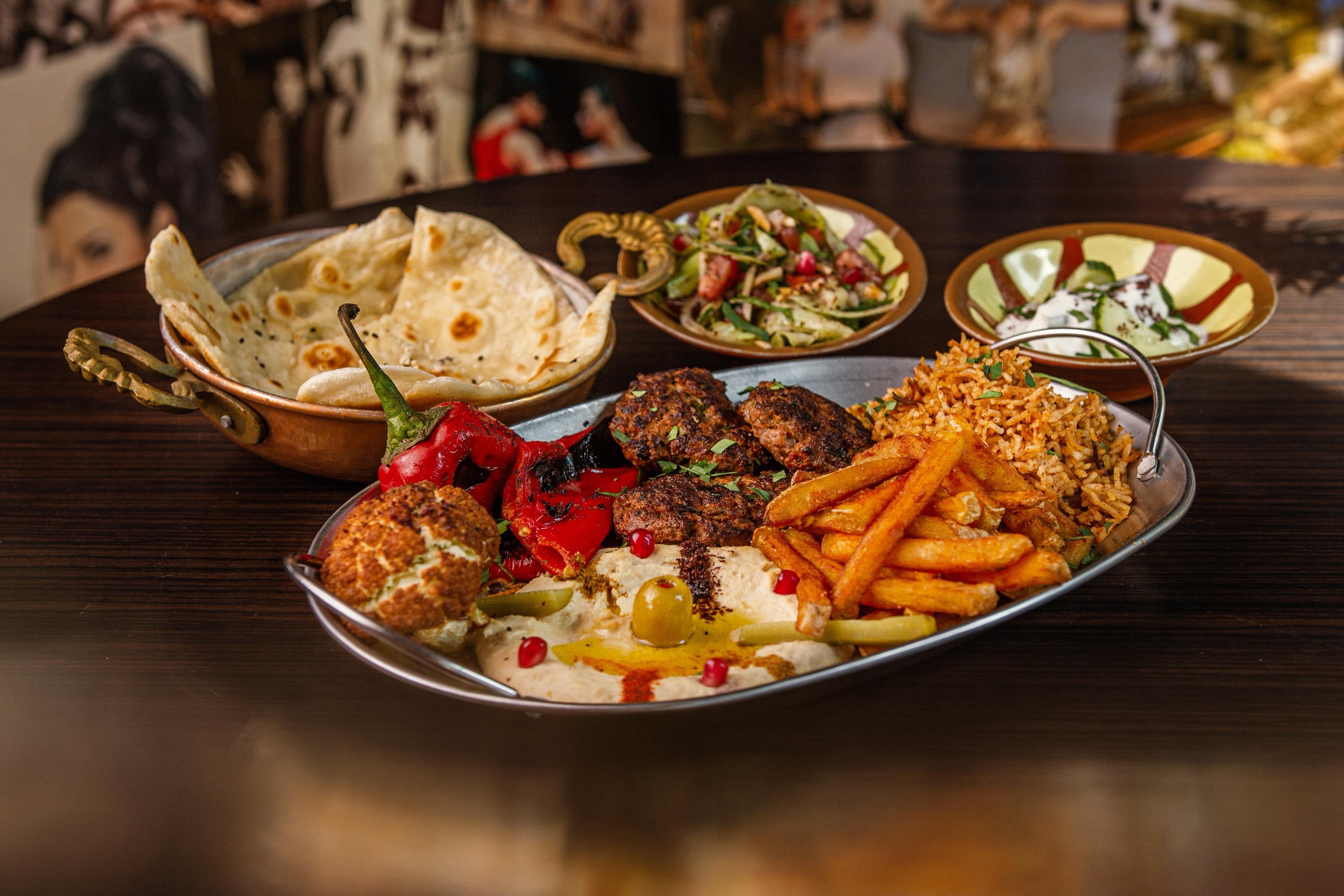 Un piatto köfte con köfte, hummus, patate a spicchi, riso, insalata, pane arabo e salsa allo yogurt.