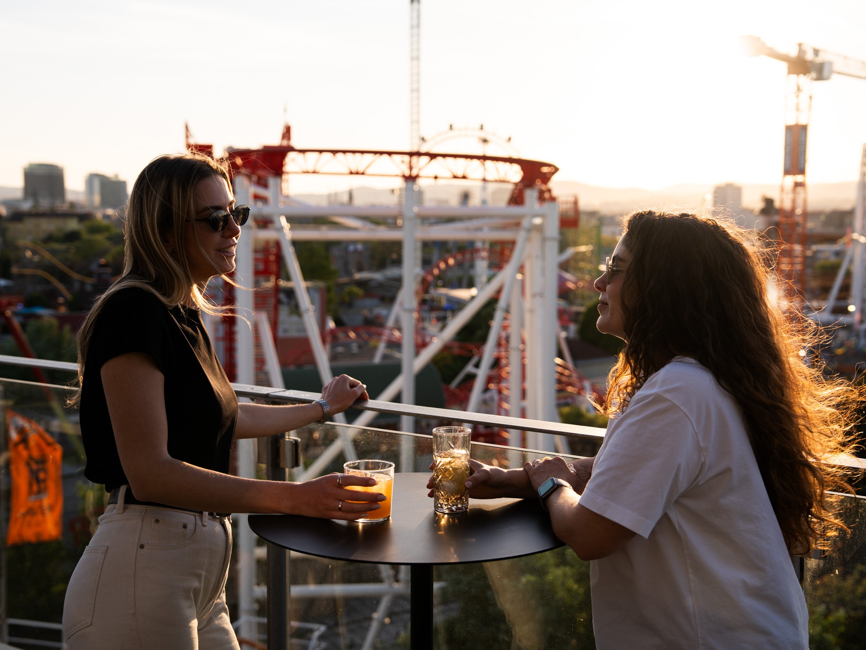 Due donne con un cocktail in mano sulla terrazza del Zoku Hotel a Vienna. Sullo sfondo il Prater al tramonto.