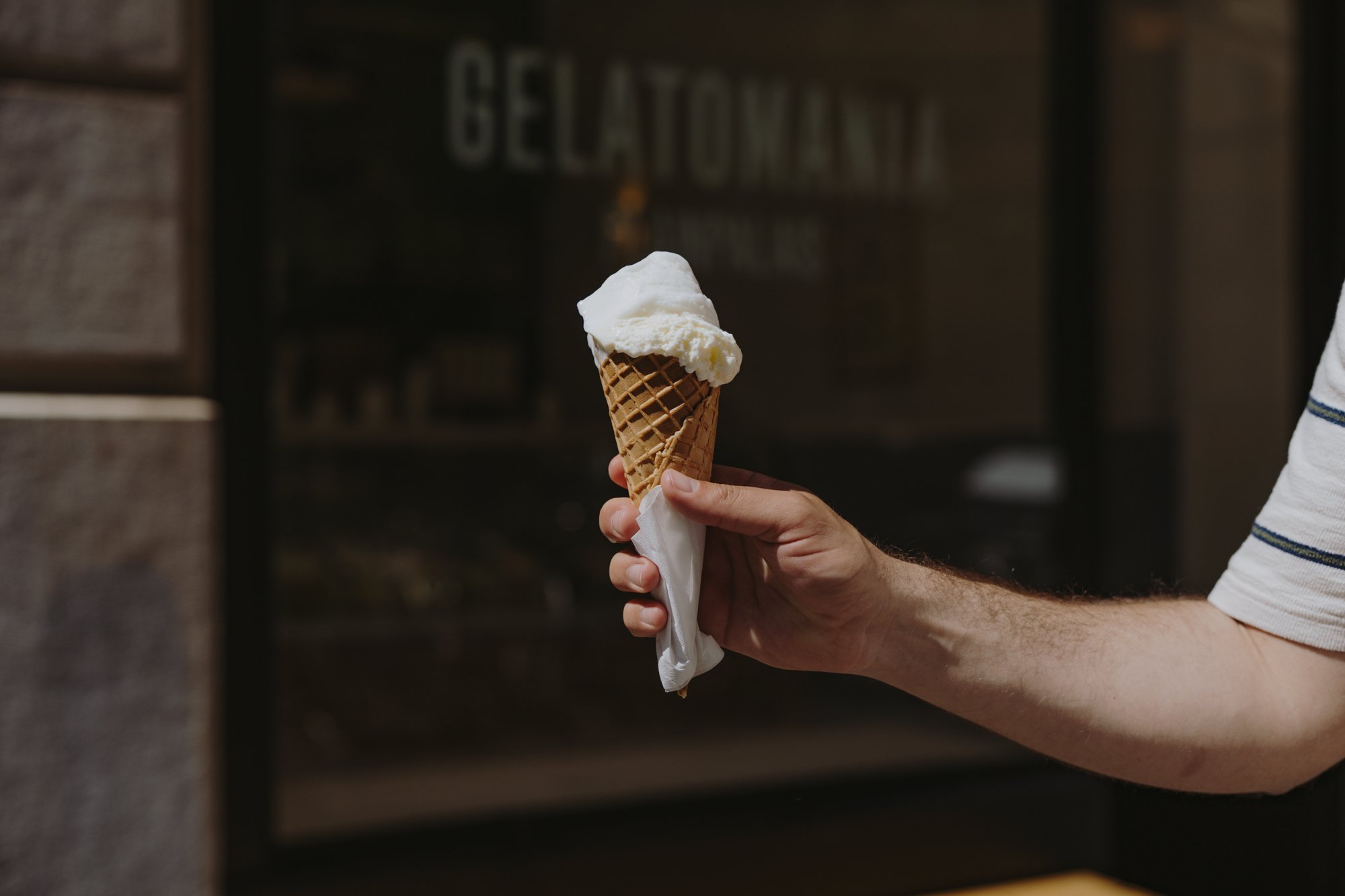 Une personne se trouve devant la vitrine du glacier Gelatomania, un cornet à la main.