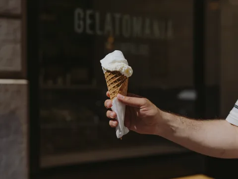 Une personne se trouve devant la vitrine du glacier Gelatomania, un cornet à la main.