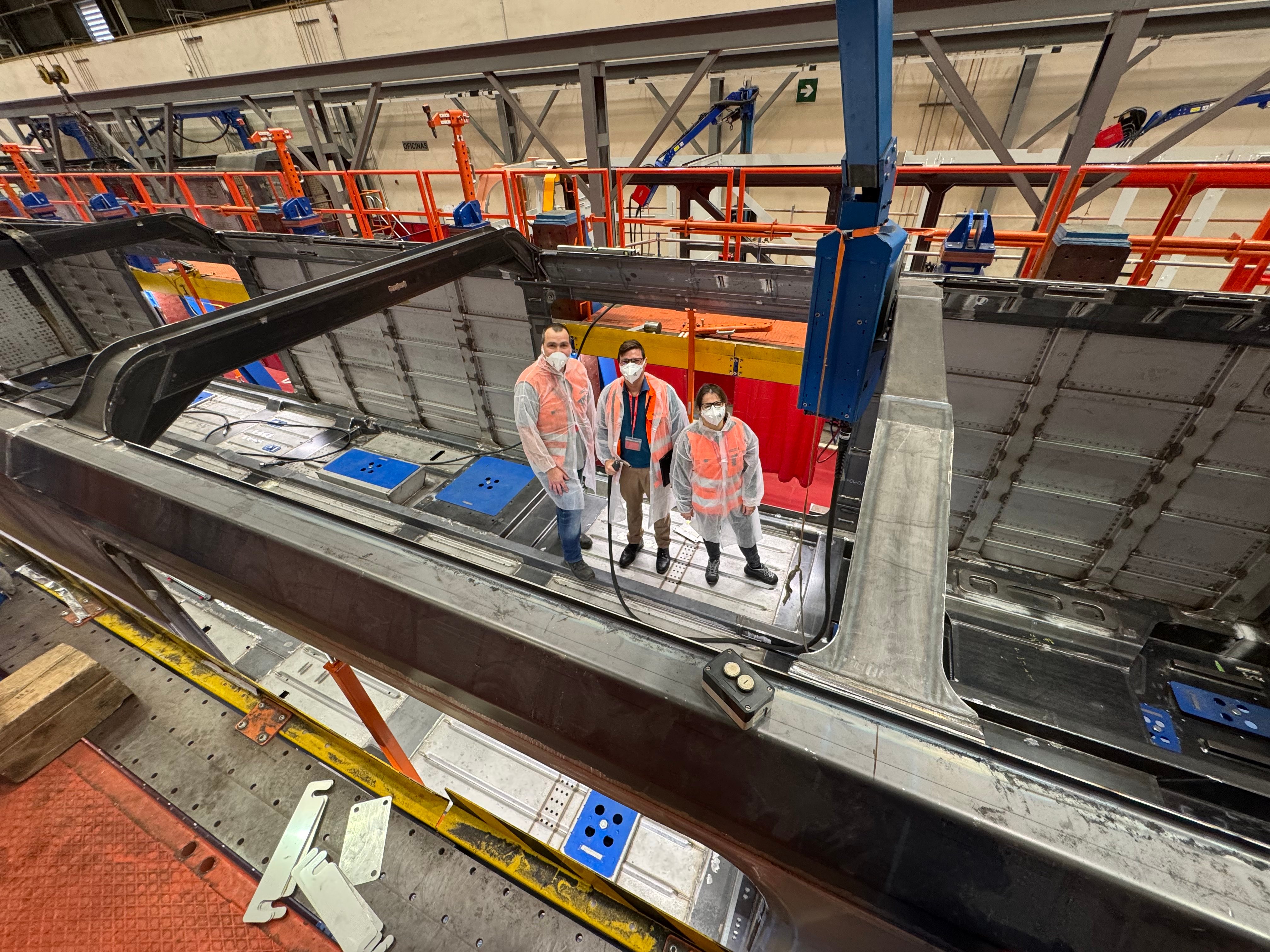 Tre collaboratori FFS lavorano alla costruzione grezza del primo prototipo. Indossano tute protettive e mascherine.