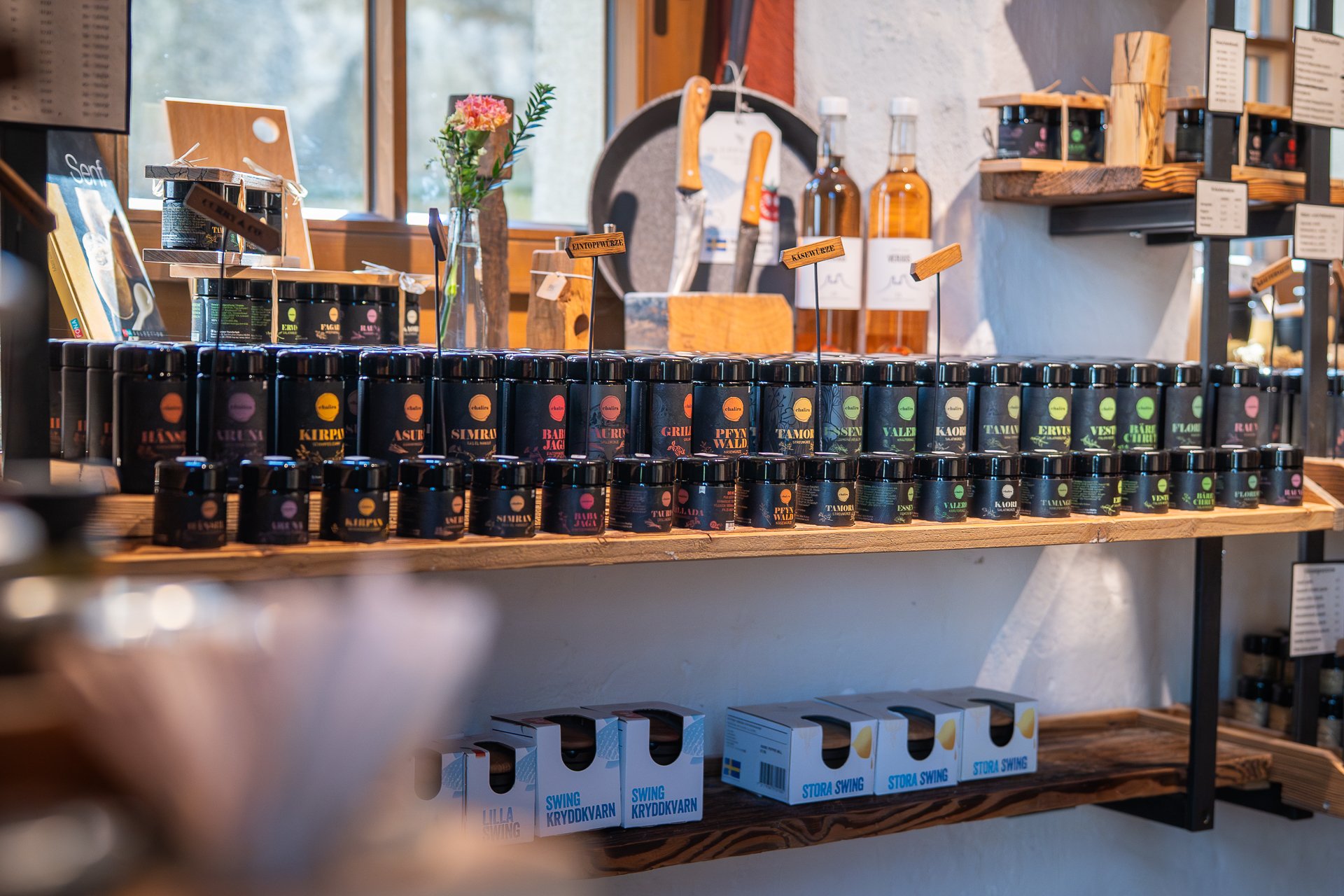 Gewürze stehen dicht aneinandergereiht auf einem Regal mit dekorativen Elementen.