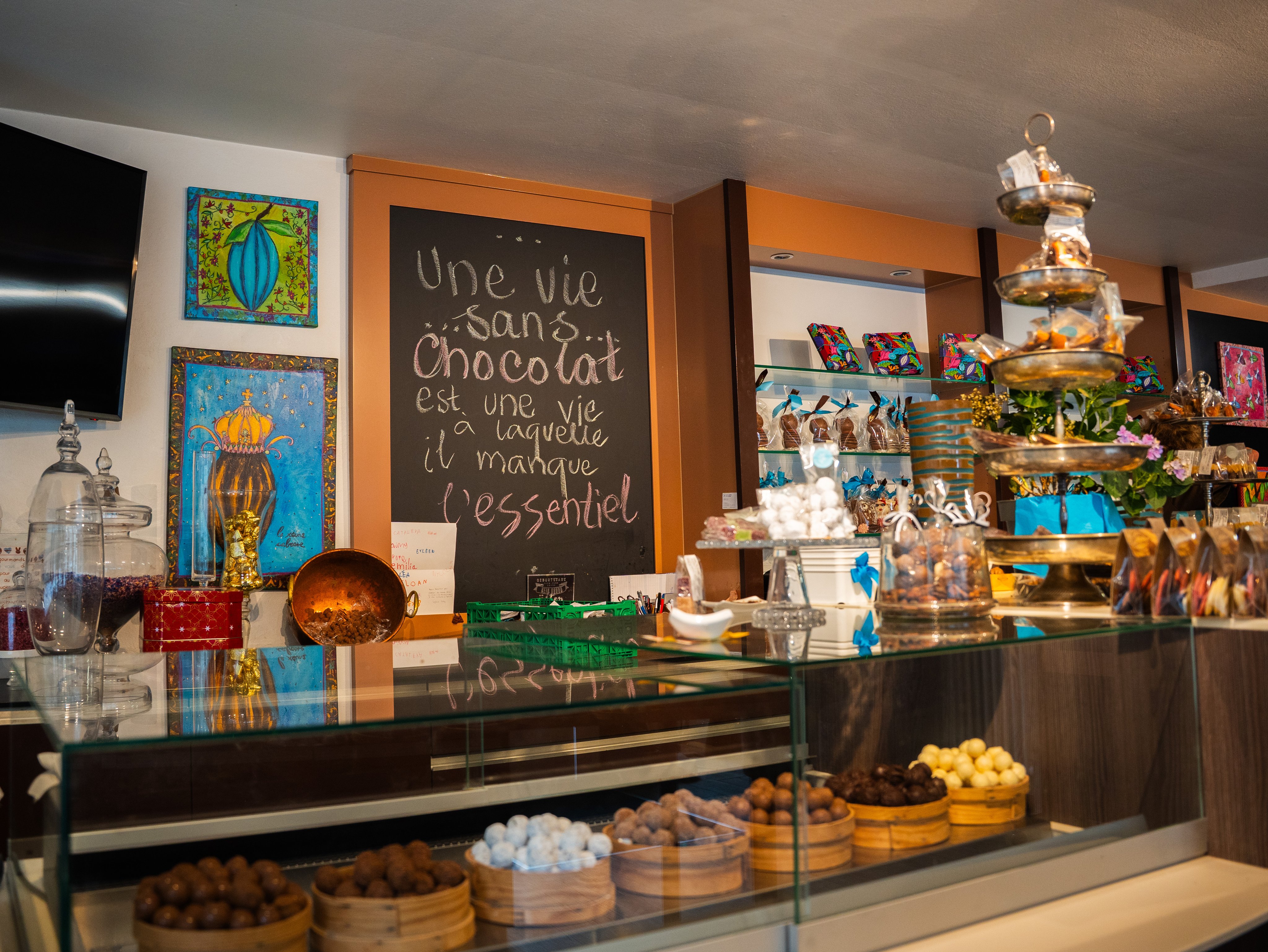 Un comptoir de magasin couvert de marchandises. À l’arrière-plan, une ardoise sur laquelle on peut lire une inscription.