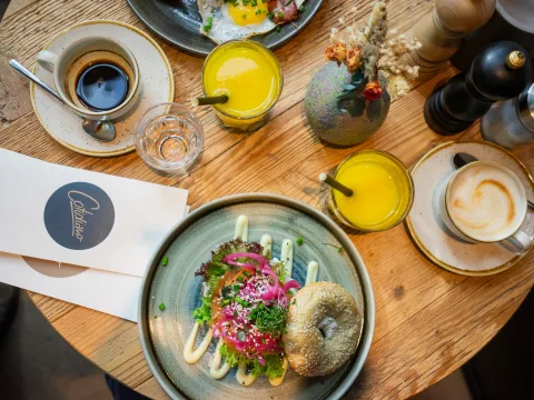 Vogelperspektive auf einen gedeckten Tisch mit Orangensaft, Kaffee und einem gut gefüllten Bagel.
