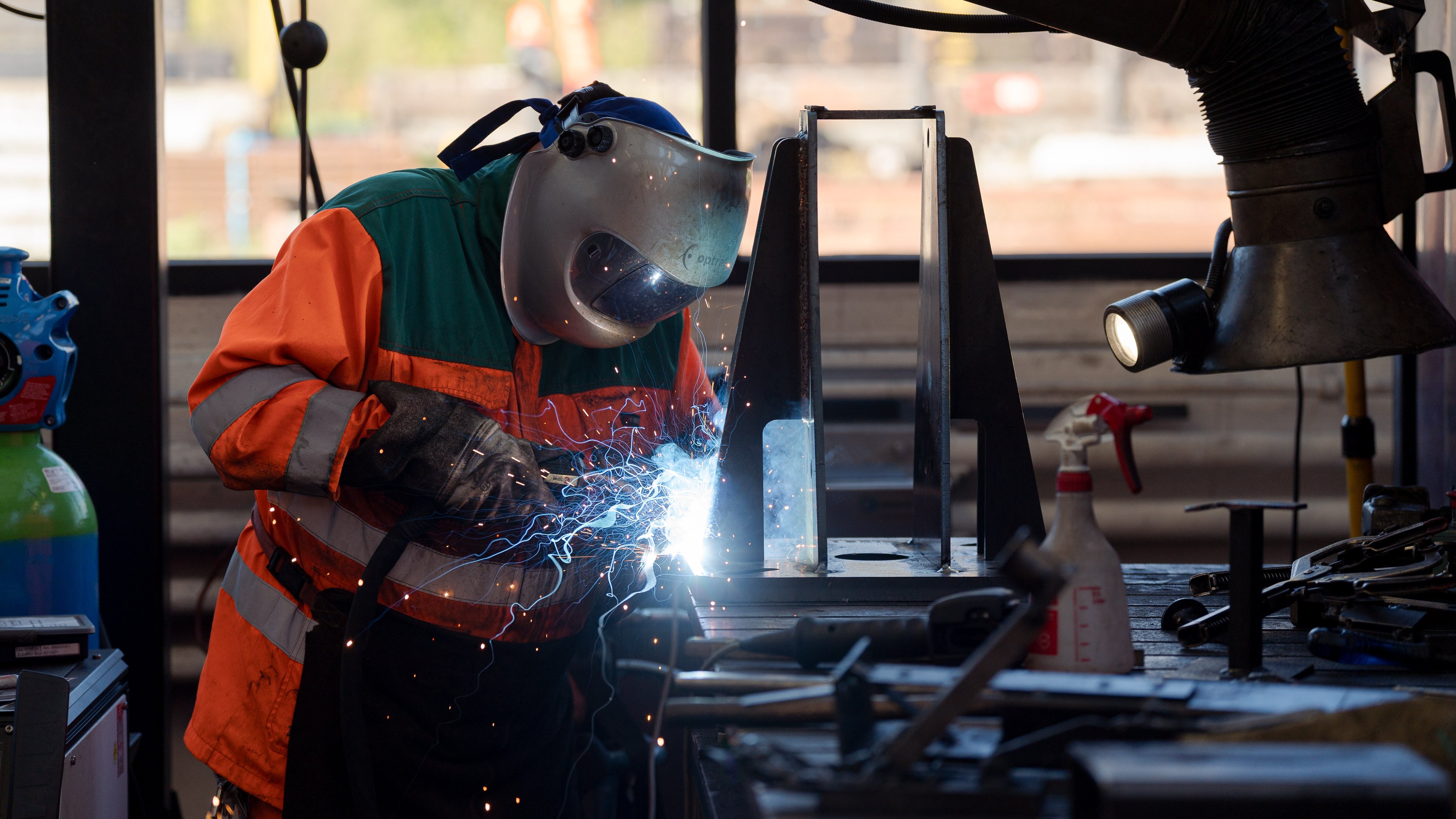 Un collaborateur soude une pièce métallique sur un établi.