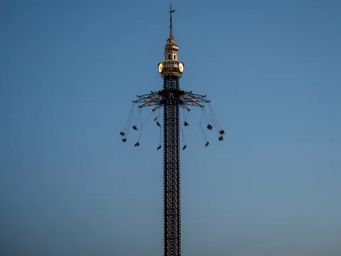 La torre del Prater illuminata con la giostra a catene in movimento si staglia sul cielo blu della sera nel Prater di Vienna.