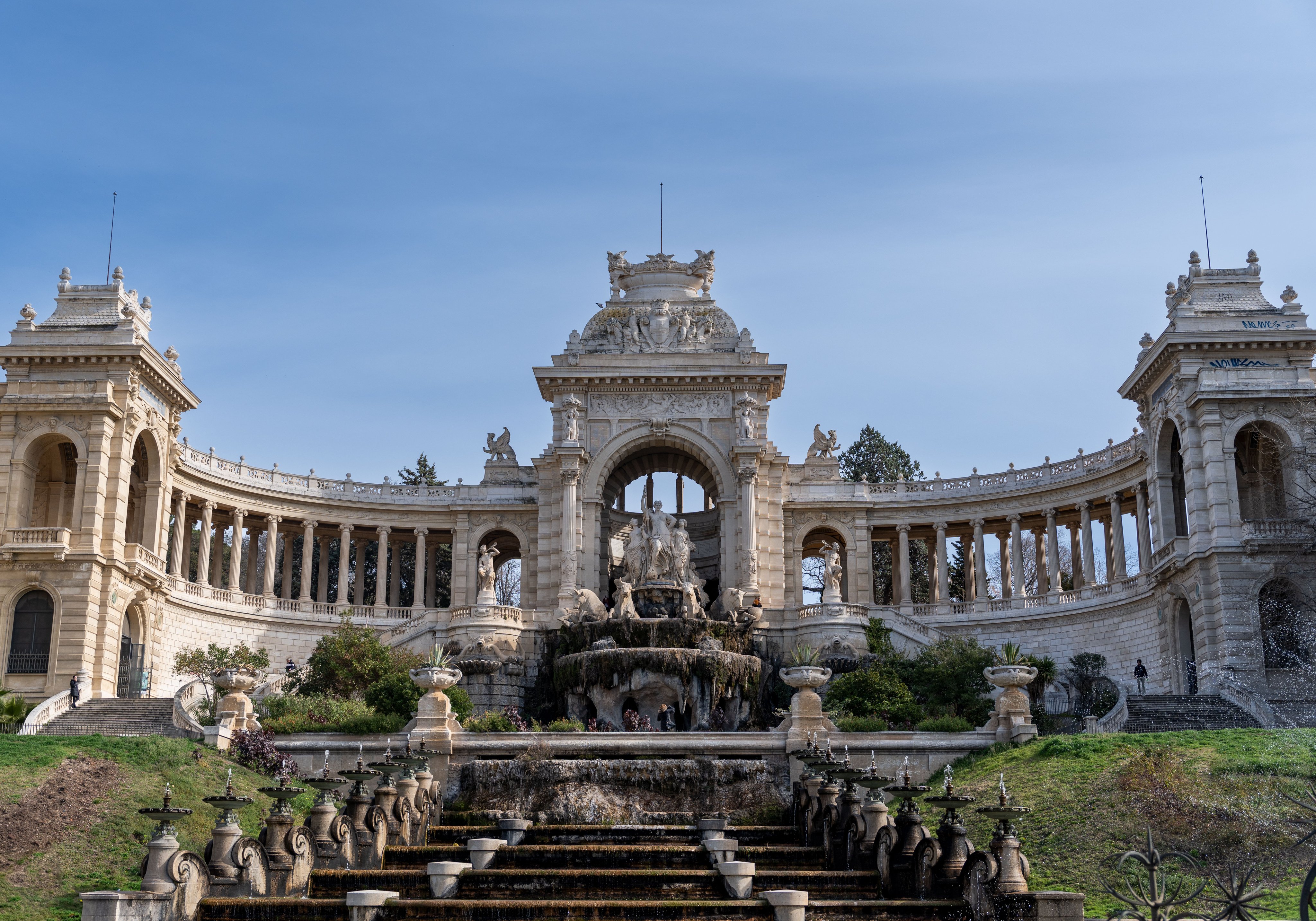 Vue du majestueux Palais Longchamp à Marseille, avec son impressionnante fontaine, ses élégantes colonnades et ses sculptures, sous un beau ciel bleu.