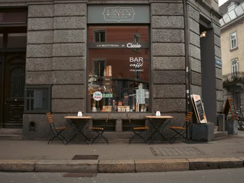 Des tables et chaises en bois se trouvent sur le chemin, devant un restaurant. Le restaurant est construit en pierres gris foncé.