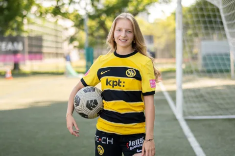 Una donna con la divisa di una squadra e un pallone sotto il braccio.