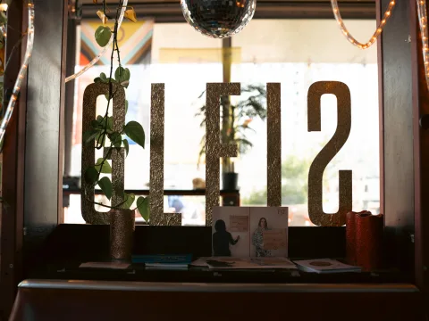 Dans le bar, devant une fenêtre, le nom Gleis est écrit en lettres dorées, entouré de bougies et de brochures sur le rebord de la fenêtre, de guirlandes lumineuses et de plantes suspendues au plafond.