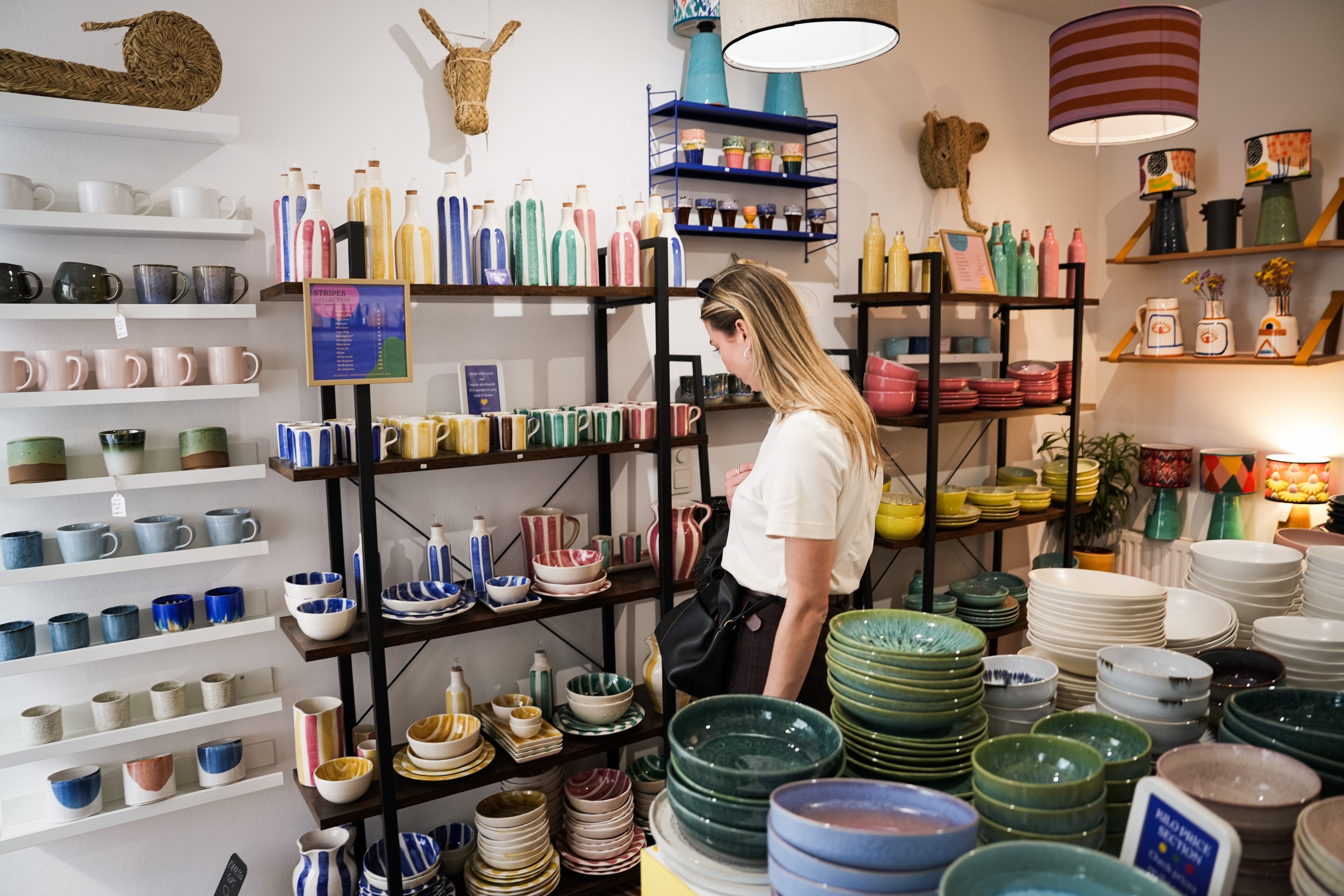 Frau betrachtet bunte Keramikschalen, Tassen und Vasen im Singulär ceramics kilo shop Wien.