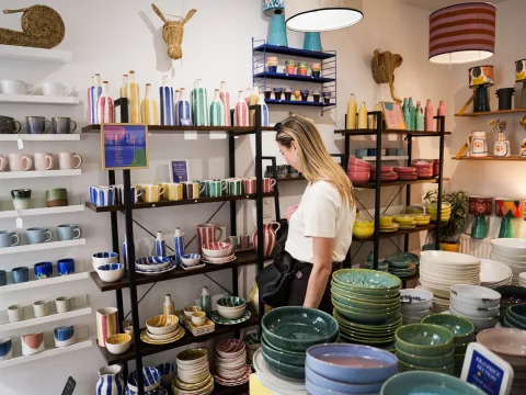 Frau betrachtet bunte Keramikschalen, Tassen und Vasen im Singulär ceramics kilo shop Wien.