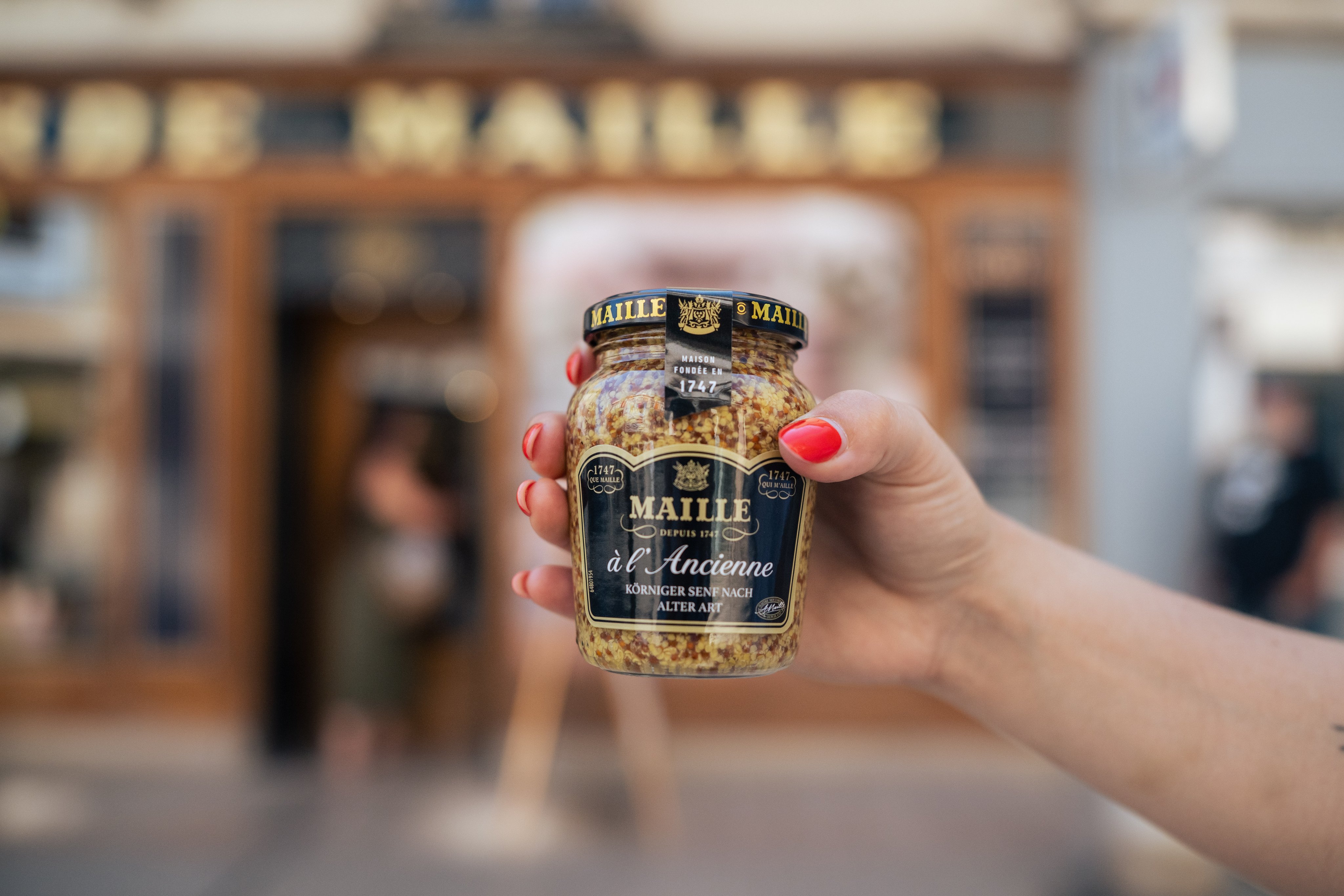 Una persona tiene in mano un barattolo di senape originale Maille, dall’inconfondibile consistenza granulosa. 