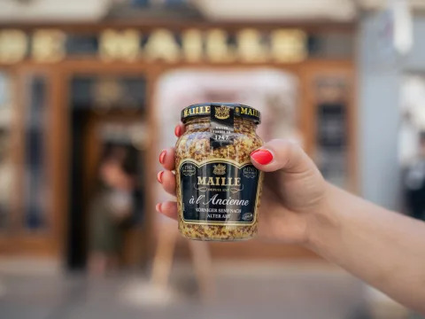 Una persona tiene in mano un barattolo di senape originale Maille, dall’inconfondibile consistenza granulosa.