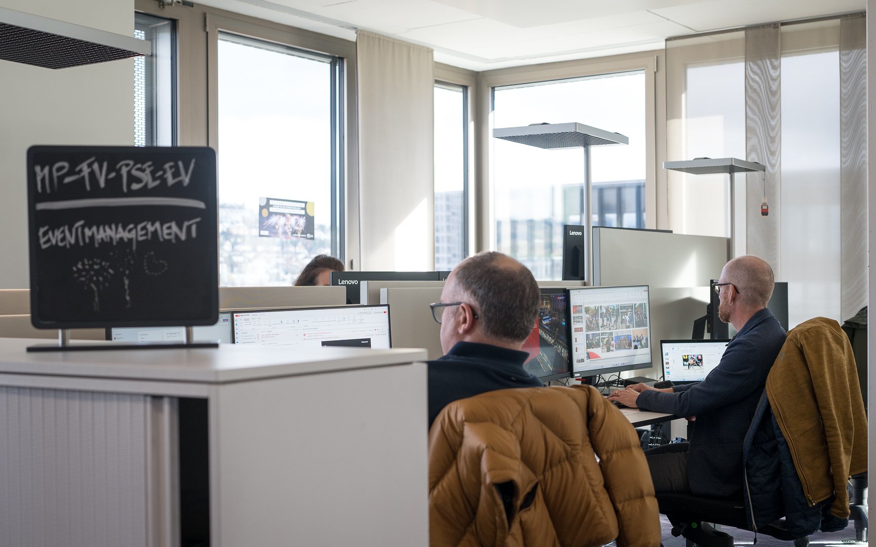 Trois personnes sont assises chacune devant un ordinateur. Le soleil brille dans le bureau.