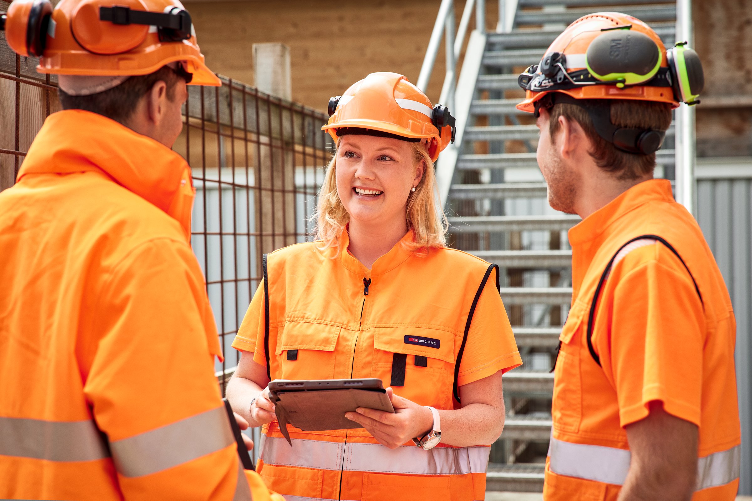 Tre persone discutono in un cantiere all’aperto.