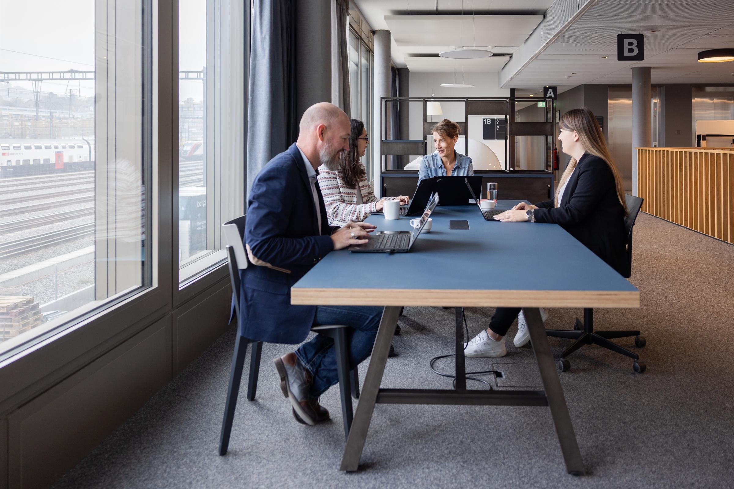 Quattro persone lavorano sedute a un tavolo blu con un computer.