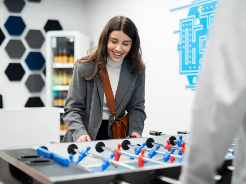 A woman plays table football and looks cheerful.