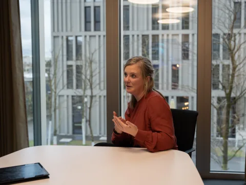 Sandra Schwander parle avec les mains tout en regardant le rédacteur pendant l’entretien. En arrière-plan, on aperçoit les voies et la gare de Wankdorf par les grandes fenêtres. L’entretien a lieu au siège des CFF.