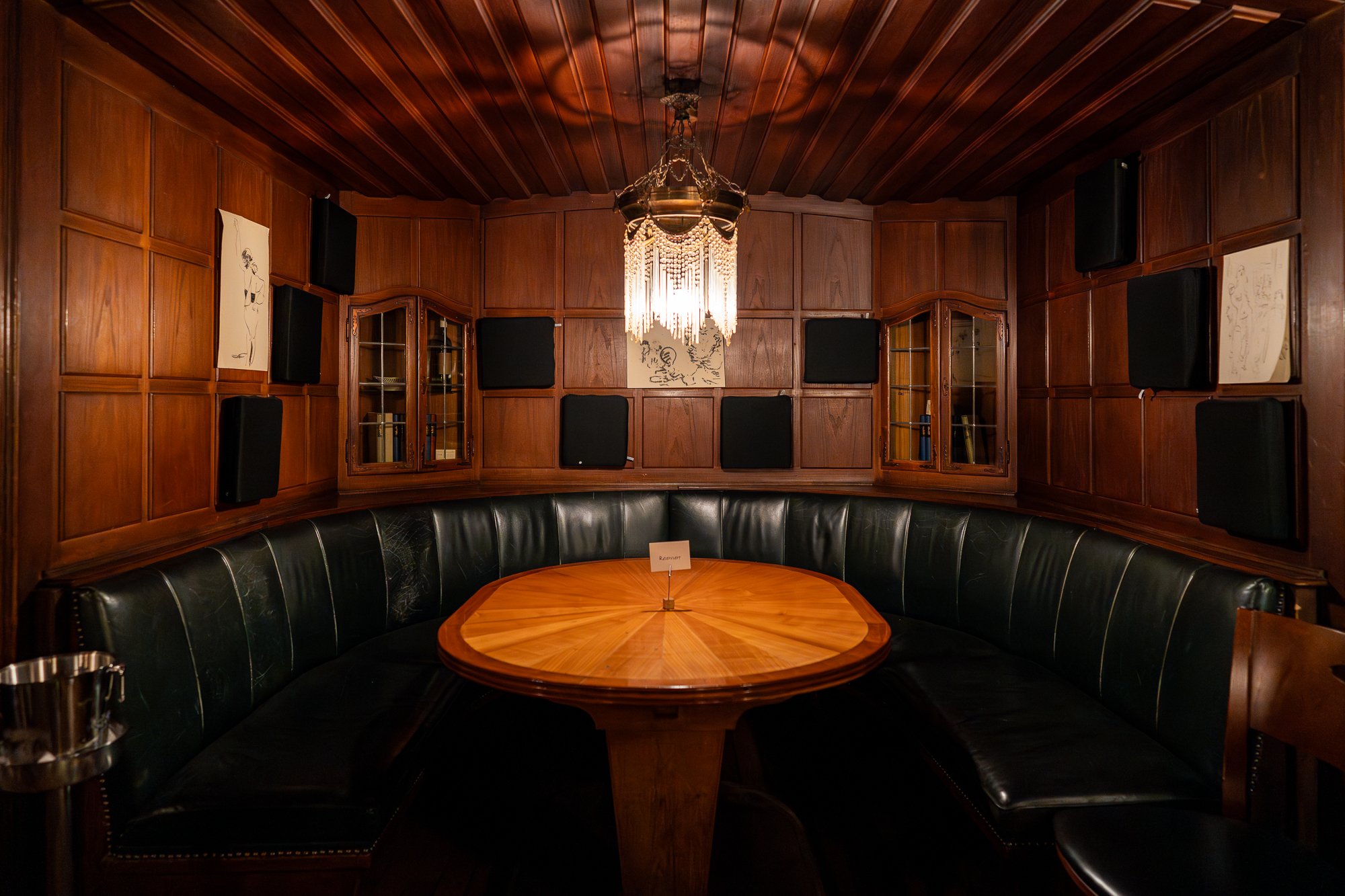 Siège vert rembourré avec une table ronde en bois au centre, entouré de murs recouverts de bois sombre.