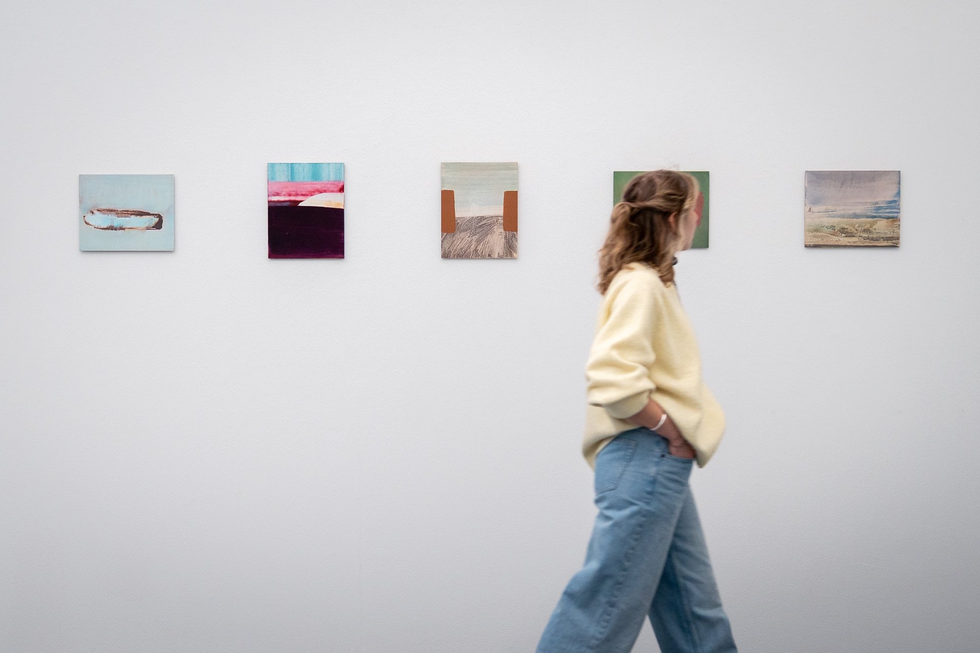 Eine Frau läuft an einer Serie von fünf Bildern vorbei.