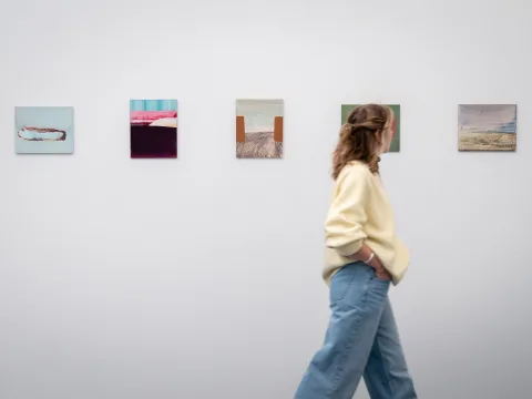 Eine Frau läuft an einer Serie von fünf Bildern vorbei.